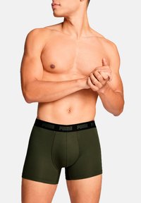 Green cotton boxer briefs with a black elastic waistband featuring the Puma logo, showcasing a fitted design and mid-thigh length.