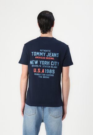 Navy blue cotton t-shirt featuring multi-colored text on the back. Text includes "TOMMY JEANS," city names, and year "1985." Casual fit.