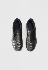 Black leather sneakers with a quilted design, featuring black laces, padded ankle collar, and a small logo on the side.