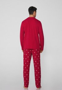 Rotes Langarmshirt kombiniert mit roten Schlafanzughosen mit Blumenmuster. Das Material wirkt weich und angenehm.