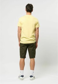 Un tricou galben cu mânecă scurtă, asociat cu pantaloni scurți cargo de culoare verde măsliniu. Ținuta prezintă un guler rotund și buzunare pe pantaloni. Se poartă adidași albi.