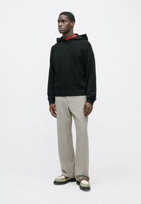 Černá texturovaná mikina s kapucí, doplněná světle šedými širokými kalhotami a robustními bílými a černými teniskami.