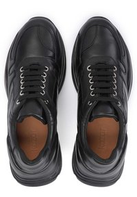 Černé kožené tenisky s texturovaným povrchem, kulatou špičkou, kovovými průchodkami a černými tkaničkami. Vnitřek je vybaven hnědou podšívkou a značkovým označením.