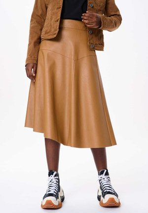 Tan faux leren midi-rok met een uitlopende vorm, met een gladde textuur en naaddetails. Gepaard met zwart-witte sneakers.