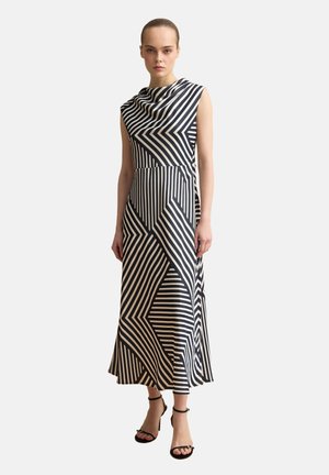 Mujer con un vestido maxi sin mangas de rayas geométricas en blanco y negro, con escote drapeado y tacones negros de pulsera al tobillo.