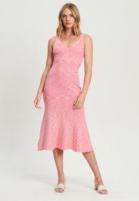 Ružová pruhovaná midi šaty s priliehavým telom, výstrihom do V a rozšíreným spodným okrajom. Vyrobené z mäkkej, rebrovanej tkaniny s textúrovaným vzorom.