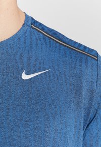 Camisa deportiva texturizada azul con el logo de Nike en blanco y una franja negra y gris a lo largo del hombro.