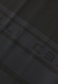 Tissu noir foncé avec un motif subtil ; présente un design de rayures horizontales proéminentes. Texture lisse ; branding minimaliste visible.