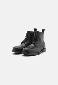 Bottines en cuir noir avec un bout arrondi, un laçage à l'avant et une fermeture éclair. Présente une semelle noire robuste et un design minimaliste.