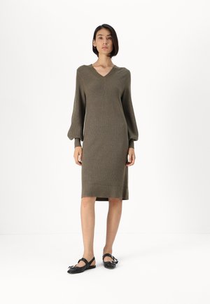 Knit dress in olive green with a V-neck, long puff sleeves, and pull-on design. Worn with black slingback shoes featuring a buckle.
