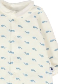 Body bianco con motivo di balene azzurro chiaro, dotato di colletto e chiusura con bottoni. Tessuto morbido con una trama liscia e piccolo marchio etichetta.