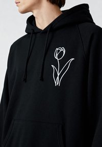 Sweat à capuche noir avec une poche frontale, orné d'un dessin de tulipe blanche brodée sur le côté gauche de la poitrine, fabriqué en tissu doux avec capuche à cordon.