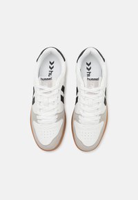 White athletic sneakers with black accents and grey suede detailing, featuring a perforated toebox, white laces, and a rubber sole.