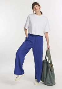 Korte witte t-shirt met opgerolde mouwen; losse blauwe broek; witte sneakers; grijze tote bag met twee handvaten; gladde textuur.