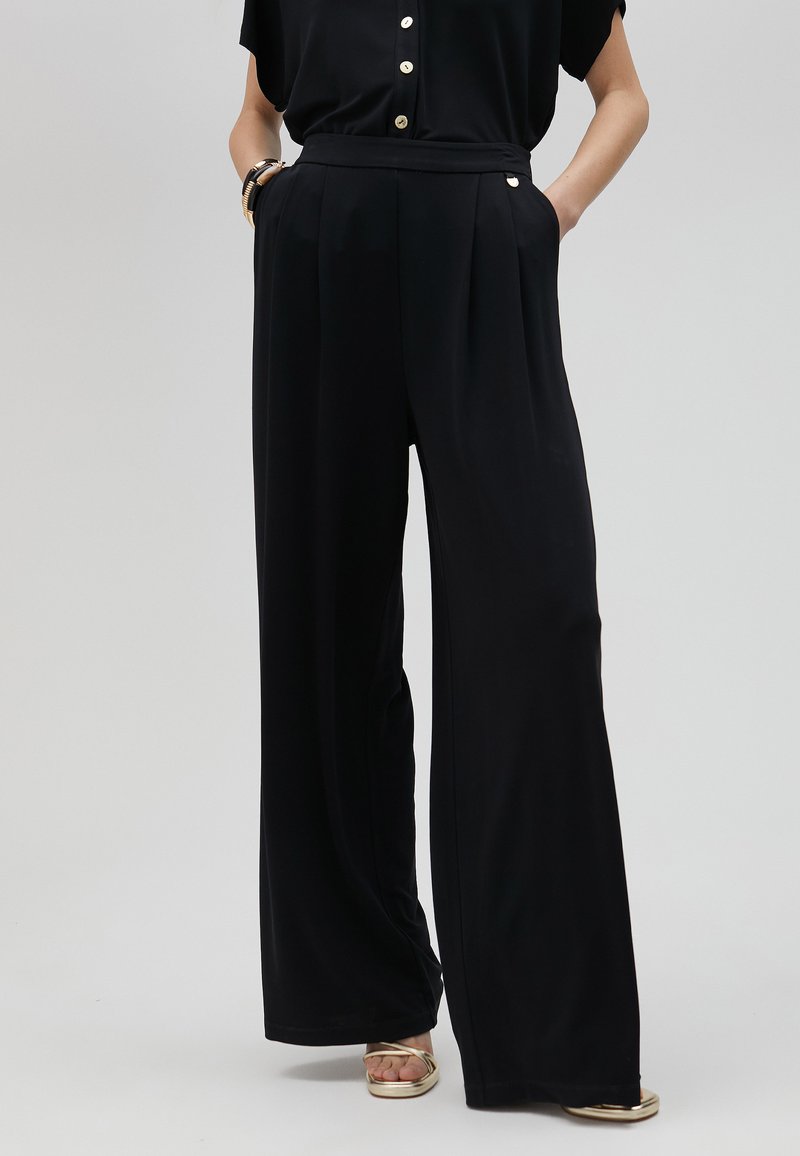 Pantalones de pierna ancha negros, confeccionados en una tela suave, con pliegues frontales, bolsillos laterales y un detalle de cinturón a juego en la cintura.