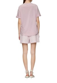 Roze t-shirt met korte mouwen en opgerolde mouwen, gecombineerd met lichtroze gestreepte shorts. Model draagt witte vetersandalen met hak.