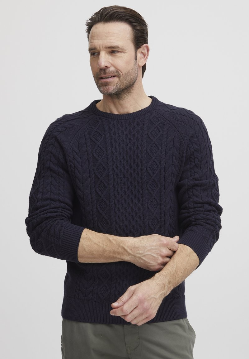 Pull en maille torsadée bleu marine avec un motif texturé, doté de bords côtelés aux poignets et au col. Le design présente un col ras du cou classique et une maille épaisse.
