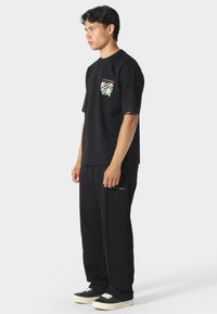 Czarna koszulka z krótkim rękawem z graficznym nadrukiem z przodu; w połączeniu z dopasowanymi czarnymi spodniami dresowymi z subtelnym złotym tekstem. Luźny krój i lekką tkanina.