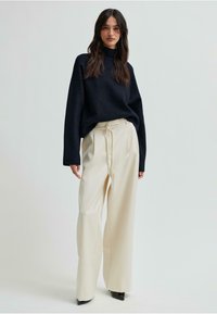 Granatowy sweter z golfem zestawiony z kremowymi spodniami o szerokich nogawkach i elastycznym pasem. Wyróżniają się gładkimi fakturami i kontrastującymi kolorami.