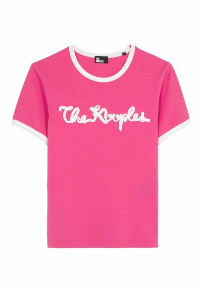Roze katoenen T-shirt met een witte ronde hals en mouwrand. Bevat "The Kooples" in witte cursieve letters over de voorkant. Korte mouwen, klassieke pasvorm.