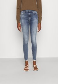 Vaqueros ajustados de denim azul claro, con una cintura de altura media, detalles desgastados, diseño de cinco bolsillos y combinados con sandalias blancas de tiras.