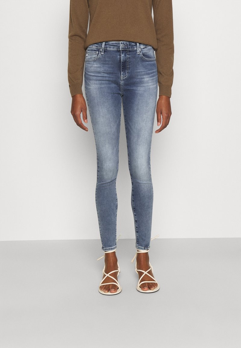 Vaqueros ajustados de denim azul claro, con una cintura de altura media, detalles desgastados, diseño de cinco bolsillos y combinados con sandalias blancas de tiras.