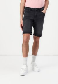 Shorts en denim gris foncé pour homme, avec une coupe classique, un design à cinq poches et des ourlets retroussés, assortis à des baskets blanches et des chaussettes légères.