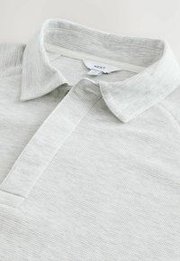 Lys grå polo shirt med et struktureret stof, en klassisk krave og en knapliste. Mærketiketten er synlig indeni kraven.