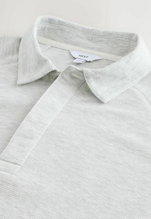 Helles graues Poloshirt aus strukturiertem Stoff, mit klassischem Kragen und Knopfleiste. Markenlabel innen am Kragen sichtbar.