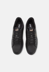 Black leather sneakers with a smooth finish, featuring black laces, padded collar, and a gold-accented logo on the side.