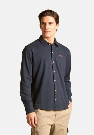 Camicia a maniche lunghe blu navy realizzata in tessuto morbido, con colletto, chiusura con bottoni e un piccolo logo ricamato sul petto.