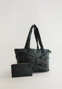 Sac fourre-tout matelassé noir avec un motif en forme de nœud et une pochette noire zippée assortie placée devant sur un fond clair.