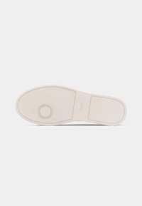 Weißer Gummisohlenschuh mit strukturierter Oberfläche, kreisförmigem Akzent und beige abgesetzten Details, der ein minimalistisches Design aufweist.