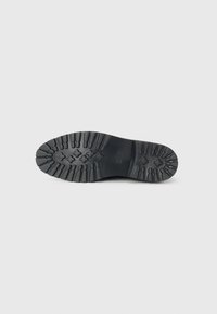 Bottes en caoutchouc noires avec une semelle texturée à crans et des rainures profondes pour une meilleure adhérence, ainsi qu'une finition lisse sur la surface de la semelle.