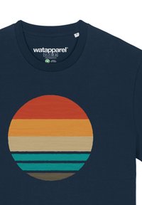 Marineblauw T-shirt met een ronde graphic van gelaagde strepen in oranje, geel, beige, turquoise en bruin, die doet denken aan een zonsondergang.