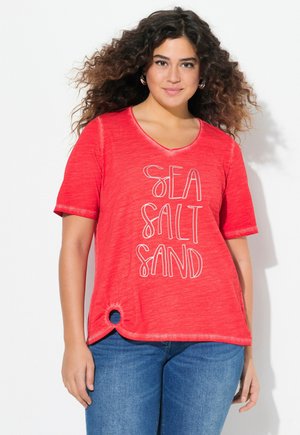 T-shirt rouge à manches courtes, arborant le texte "SEA SALT SAND" en blanc. Accent circulaire remarquable sur l'ourlet. Tissu doux et texturé.