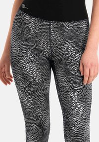 Leggings in bianco e nero con un motivo testurizzato a pelle di serpente. Vita elasticizzata e design aderente. Tessuto liscio con una leggera lucentezza.