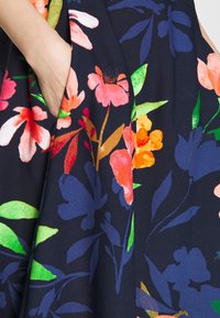 Tissu à motifs floraux en marine, présentant des fleurs vives roses, orange et vertes. Comprend une poche latérale et une texture lisse.