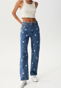 Světle modré džínsy s výšivkou květin, přímým střihem a středním pasem. V kombinaci s bílým zkráceným topem a bílými teniskami.