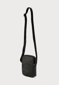 Μαύρη τσάντα χιαστί με ορθογώνιο σχήμα, λεία ματ υφή, ρυθμιζόμενο λουράκι και ασημένια λεπτομέρεια υλικού κοντά στο φερμουάρ.