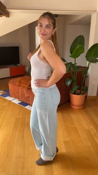 Šviesiai mėlyni plačios kojos džinsai su sukta apačia, derinami su balta, dryžuota tank top marškinėliais, kurių apvadas puoštas nėriniais. Vidinė aplinka su mediniais grindimis.