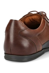 Brązowy skórzany but z perforowanym wzorem, gładką fakturą, zaokrąglonym obcasem, kontrastującą czarną podeszwą i przeszyciami z tyłu.