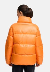 Orange puffjacka med hög krage, quiltat mönster och glänsande yta. Har voluminösa ärmar och en oversize passform.