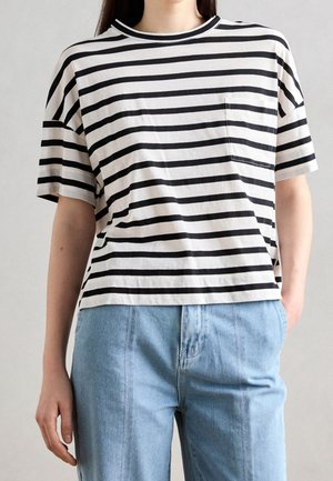 Frau trägt ein schwarz-weiß gestreiftes T-Shirt mit kleinem Brusttaschen und hellblaue hoch taillierte Jeans.