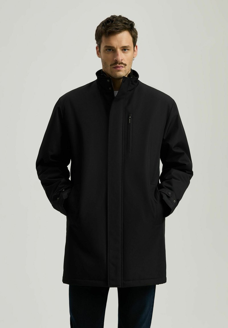 Czarny płaszcz z wysokim kołnierzem, zamykana na zamek kieszeń na piersi, kieszenie po bokach i mankiety zapinane na guziki. Gładka tekstura, średniej długości fason.