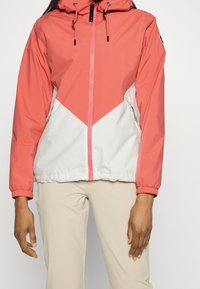 Chaqueta cortavientos en coral y blanco, con diseño en cheurón, capucha ajustable con cordones y bolsillos laterales con cremallera.