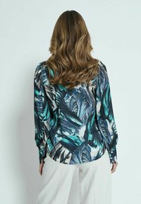 Blusa de manga larga con un vibrante estampado de hojas en azul verdoso, negro y crema; tejido suave con un corte holgado y puños abotonados.