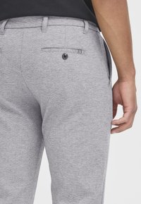 Grå, strukturerede bukser med en baglomme med knaplukning og bæltestrop, designet til en tætsiddende pasform.