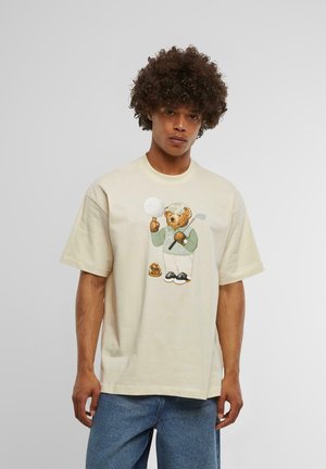 Beige cotton t-shirt featuring a cartoon bear dressed in golf attire, holding a golf club and ball, with a playful design and relaxed fit.