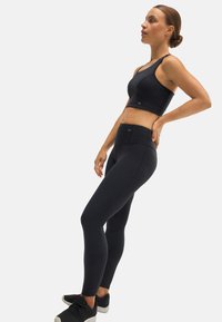 Sujetador deportivo negro con un diseño sin costuras y tirantes anchos, combinado con leggings negros de cintura alta. Ambas prendas están hechas de una tela elástica.